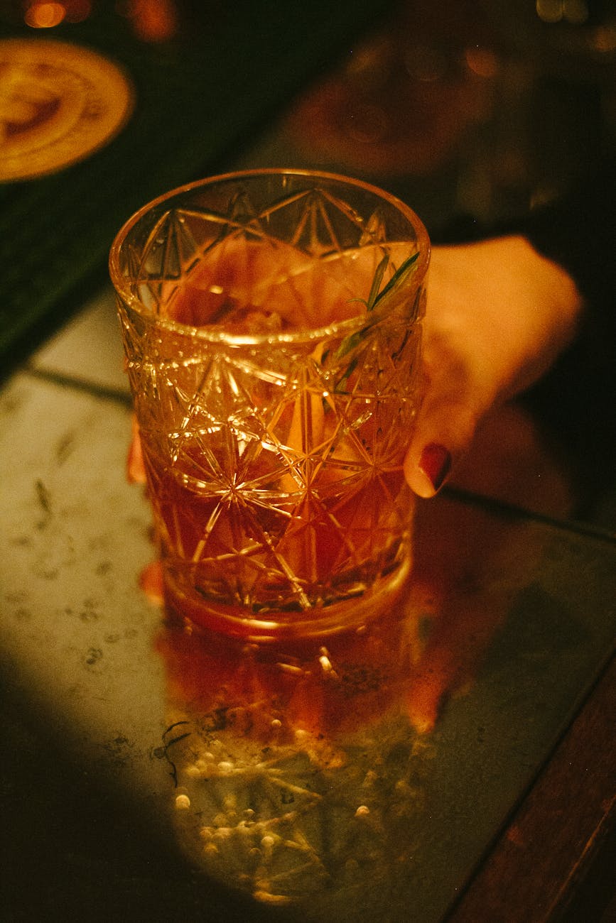 Hand holding a craft cocktail in a dimly lit speakeasy bar