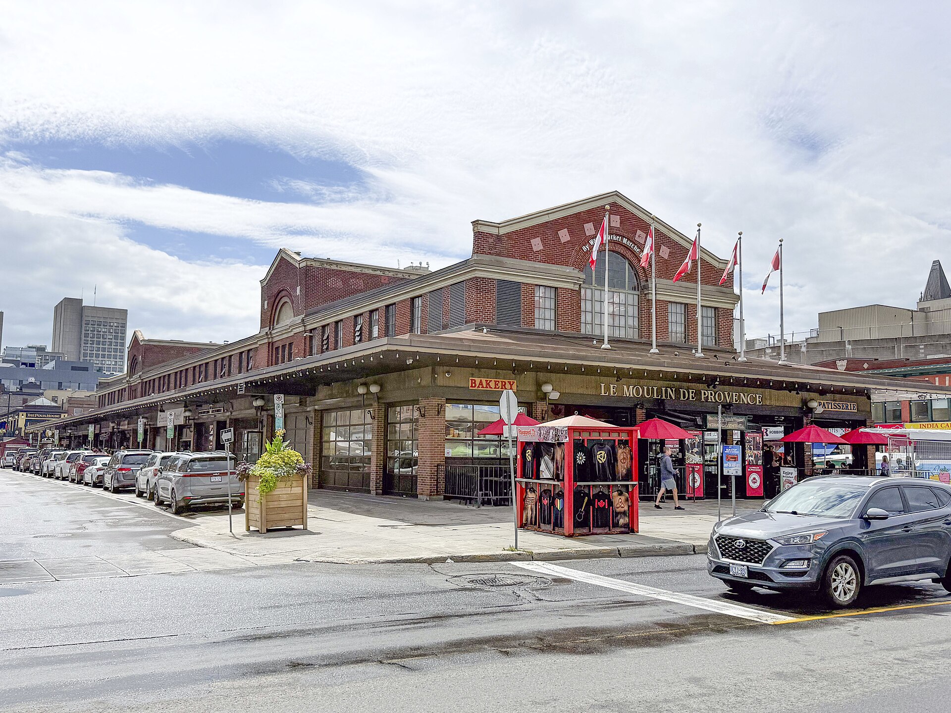 The red-brick ByWard Market building in Ottawa with Canadian flags on the roof, a bakery and red patio umbrellas at street level