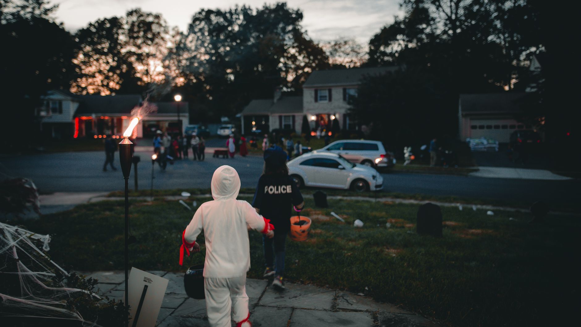 Children in costume carrying buckets along a residential street at twilight