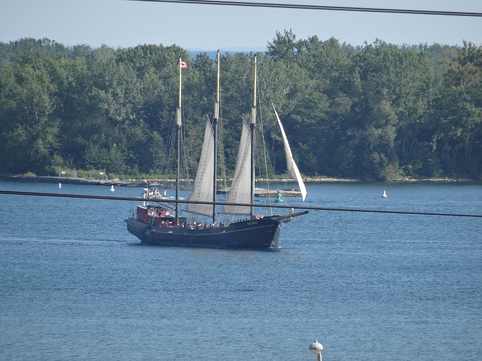 Three-masted schooner Kajama sailing in Toronto Harbour with the wooded shore of the Toronto Islands behind