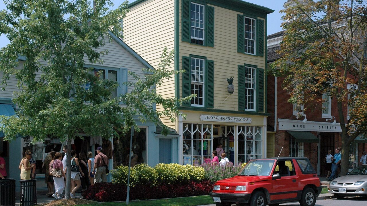 Historic clapboard shopfronts with green shutters and flower beds on Queen Street in Niagara-on-the-Lake