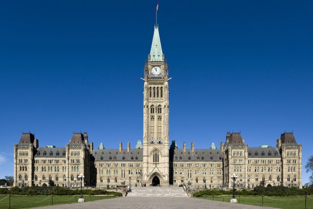 The Gothic Revival Centre Block of Canada's Parliament in Ottawa, with the Peace Tower rising in the middle under a deep blue sky