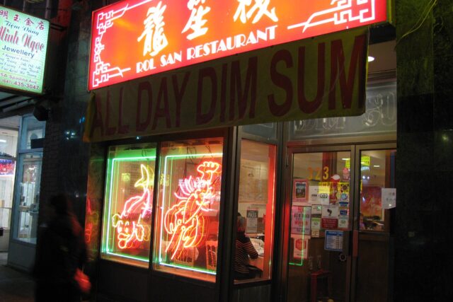 The neon-lit storefront of Rol San Restaurant on Spadina Avenue at night, with an All Day Dim Sum banner and glowing lobster and fish signs in the window