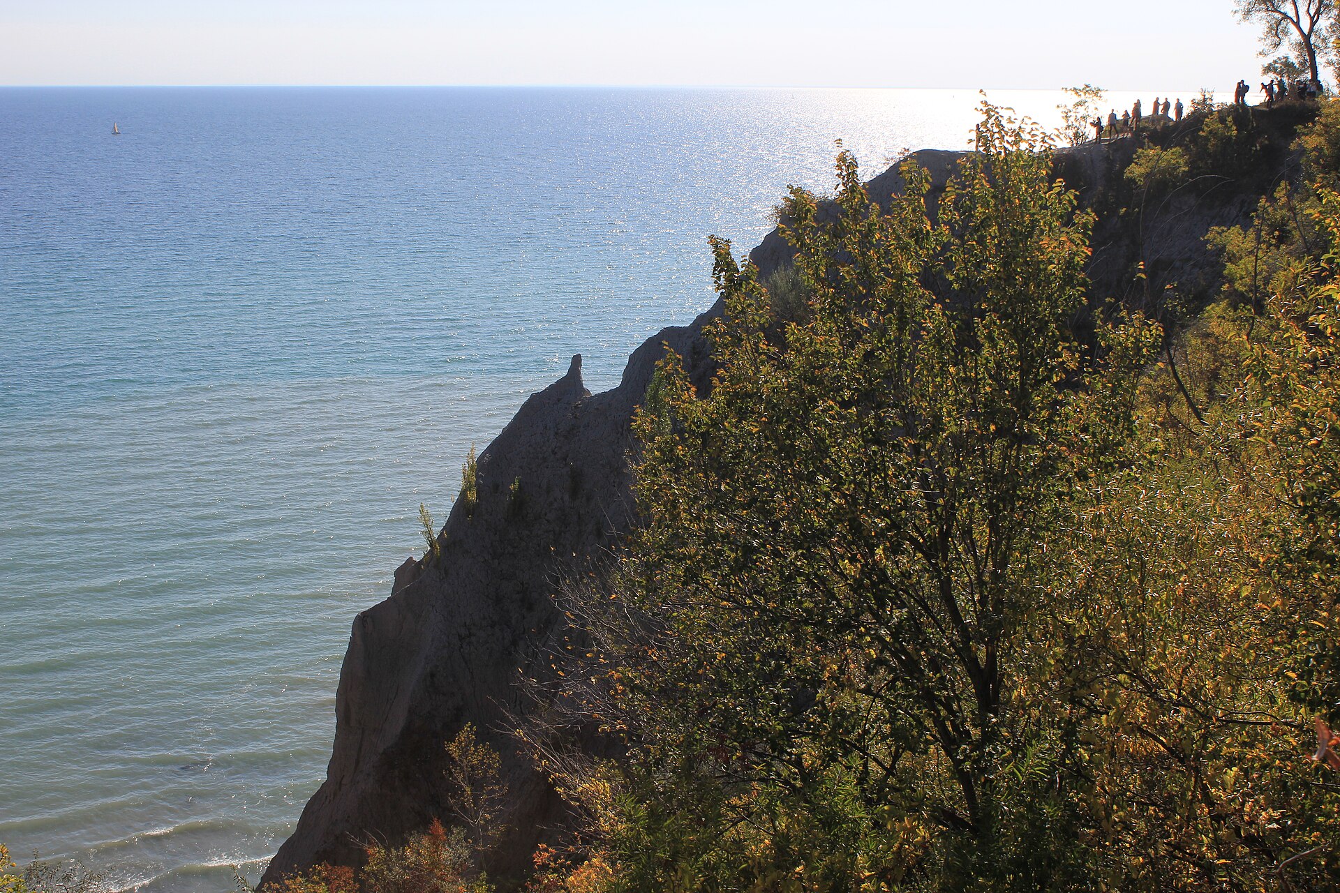 View along the top of the Scarborough Bluffs in autumn with people standing near the unfenced cliff edge above Lake Ontario