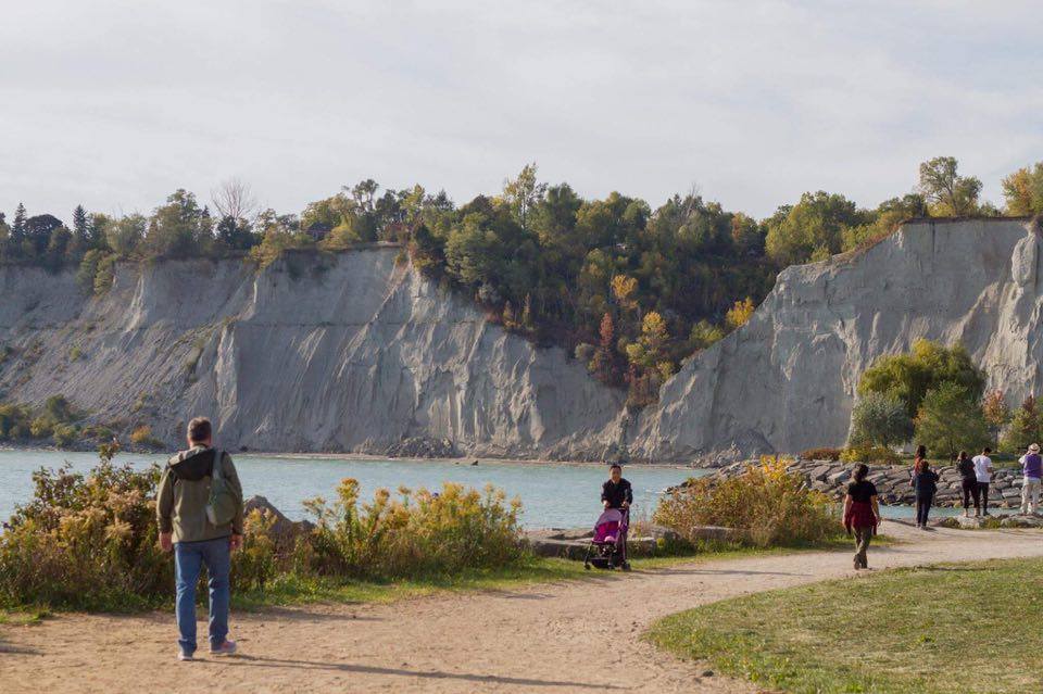 White cliffs of the Scarborough Bluffs above a shoreline path in autumn with walkers and Lake Ontario