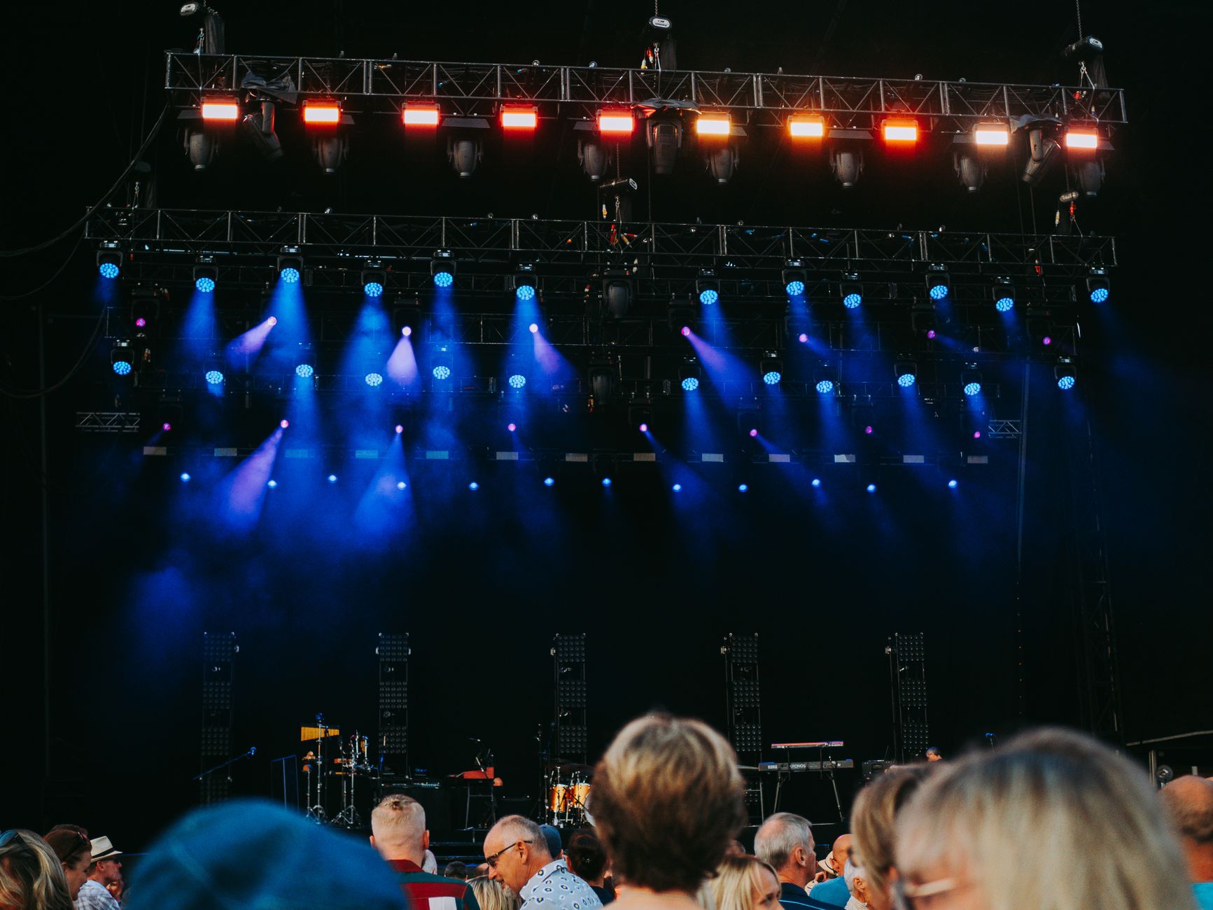 A concert crowd with arms raised in front of a brightly lit arena stage