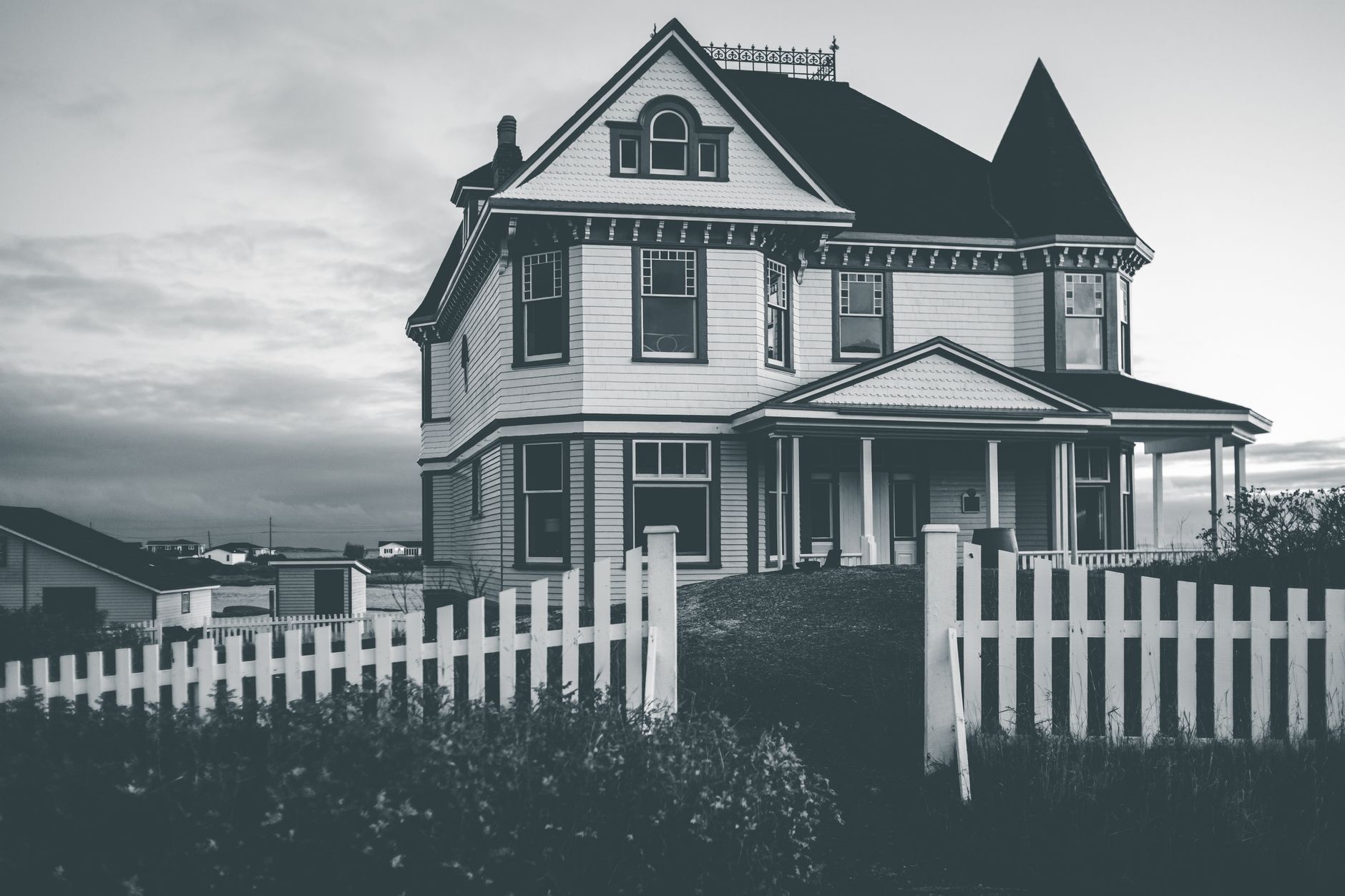 A clapboard house behind a picket fence under a heavy sky