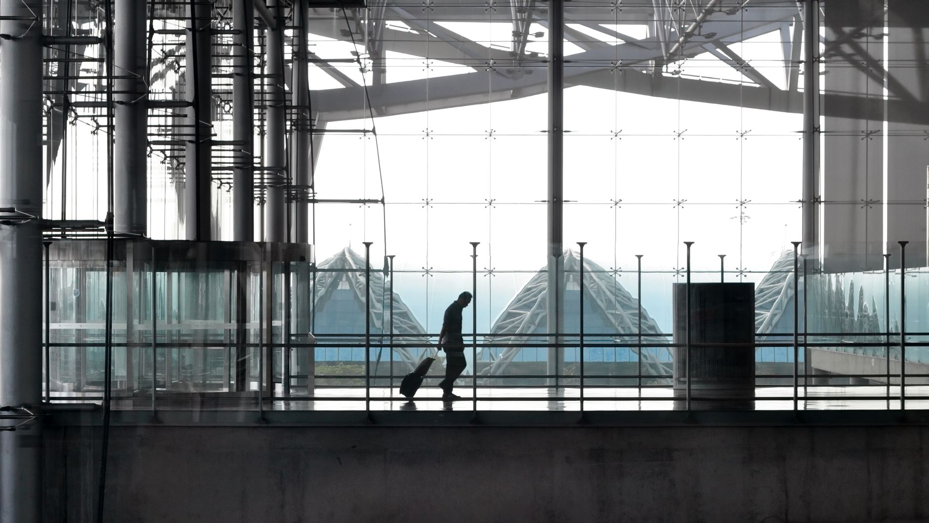 Traveller pulling a wheeled suitcase through a bright airport terminal concourse