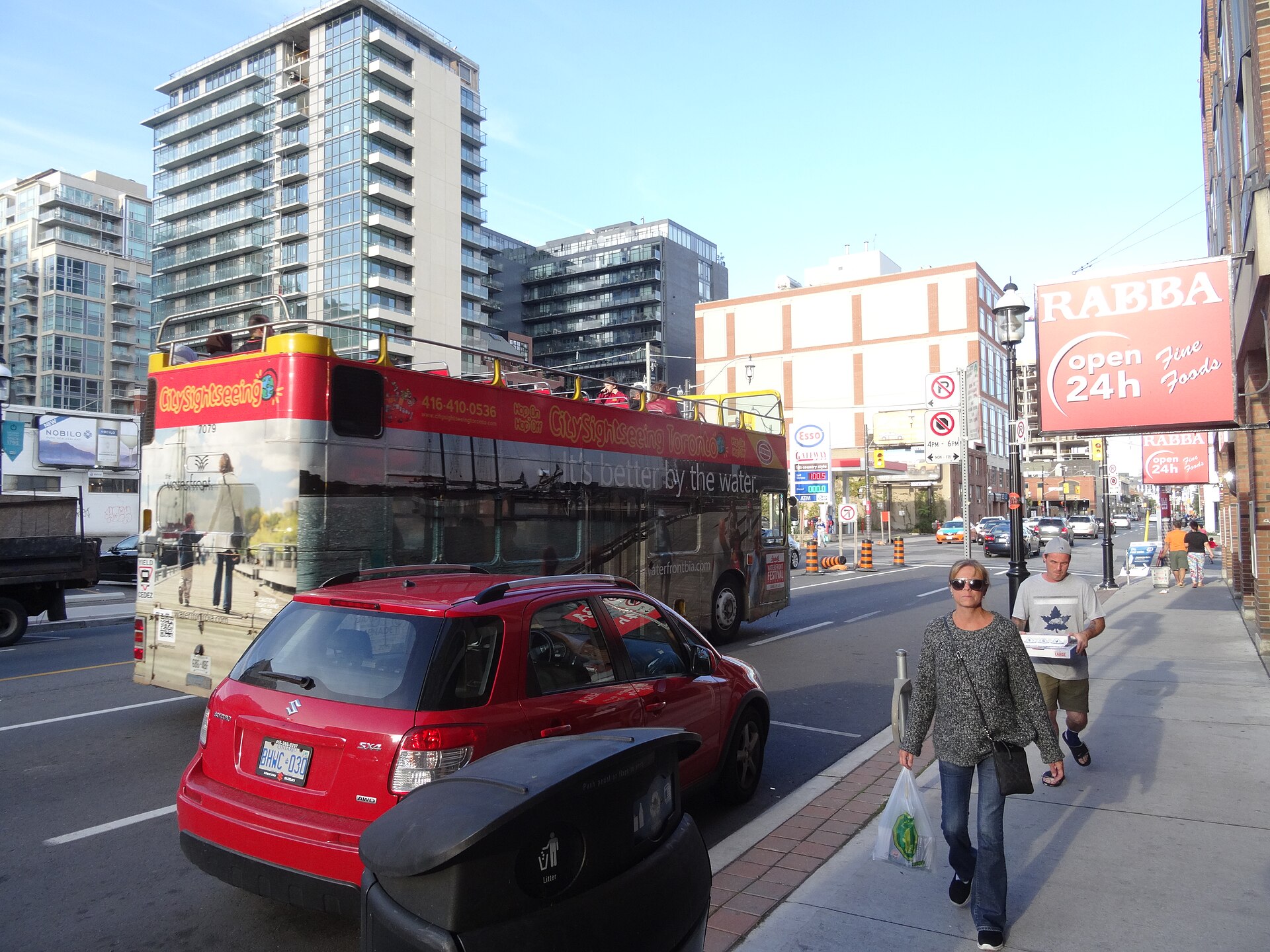 Red open-top double-decker sightseeing bus stopped in downtown Toronto traffic with passengers on the upper deck