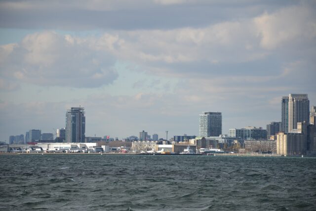 Billy Bishop Toronto City Airport seen across choppy Lake Ontario, with parked aircraft, the ferry, waterfront condo towers and the old grain silos under a cloudy sky