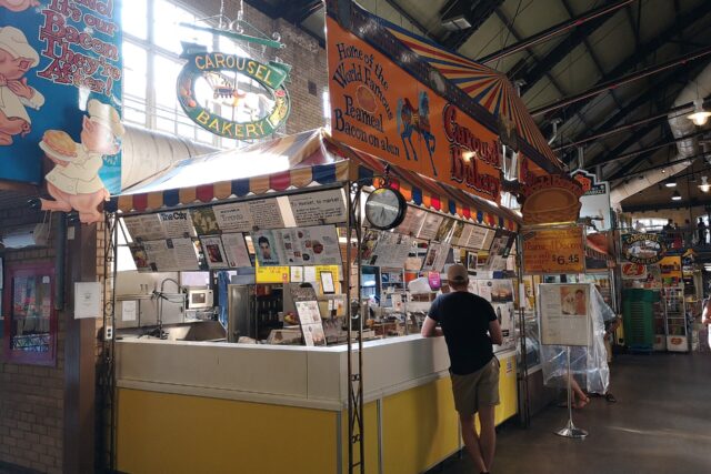 The Carousel Bakery stall in St Lawrence Market with its orange sign reading Home of the World Famous Peameal Bacon on a Bun and a customer at the counter