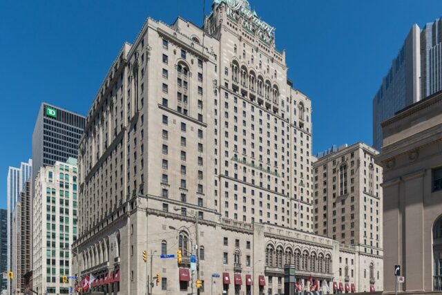 The Fairmont Royal York hotel's limestone tower on Front Street West, with the Union Station entrance sign in the foreground on a sunny day