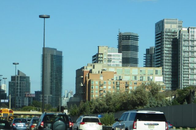 Eastbound traffic on the Gardiner Expressway approaching Humber Bay condo towers in Toronto, with an overhead travel-time sign