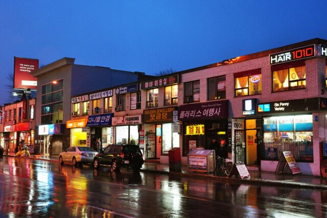 Bloor Street West in Toronto's Koreatown at dusk after rain, with lit Korean-language shop signs and reflections on the wet road