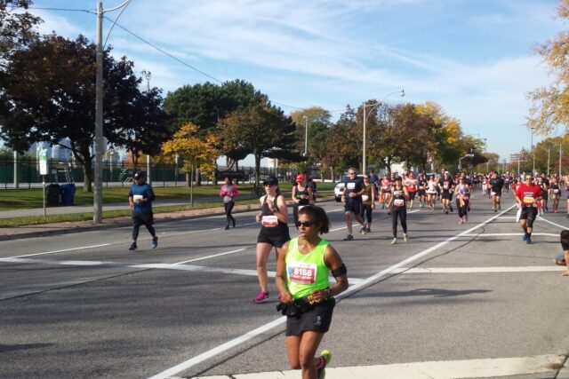 Runners follow a broad Toronto road past autumn trees and orange cones during the 2017 Toronto Waterfront Marathon.