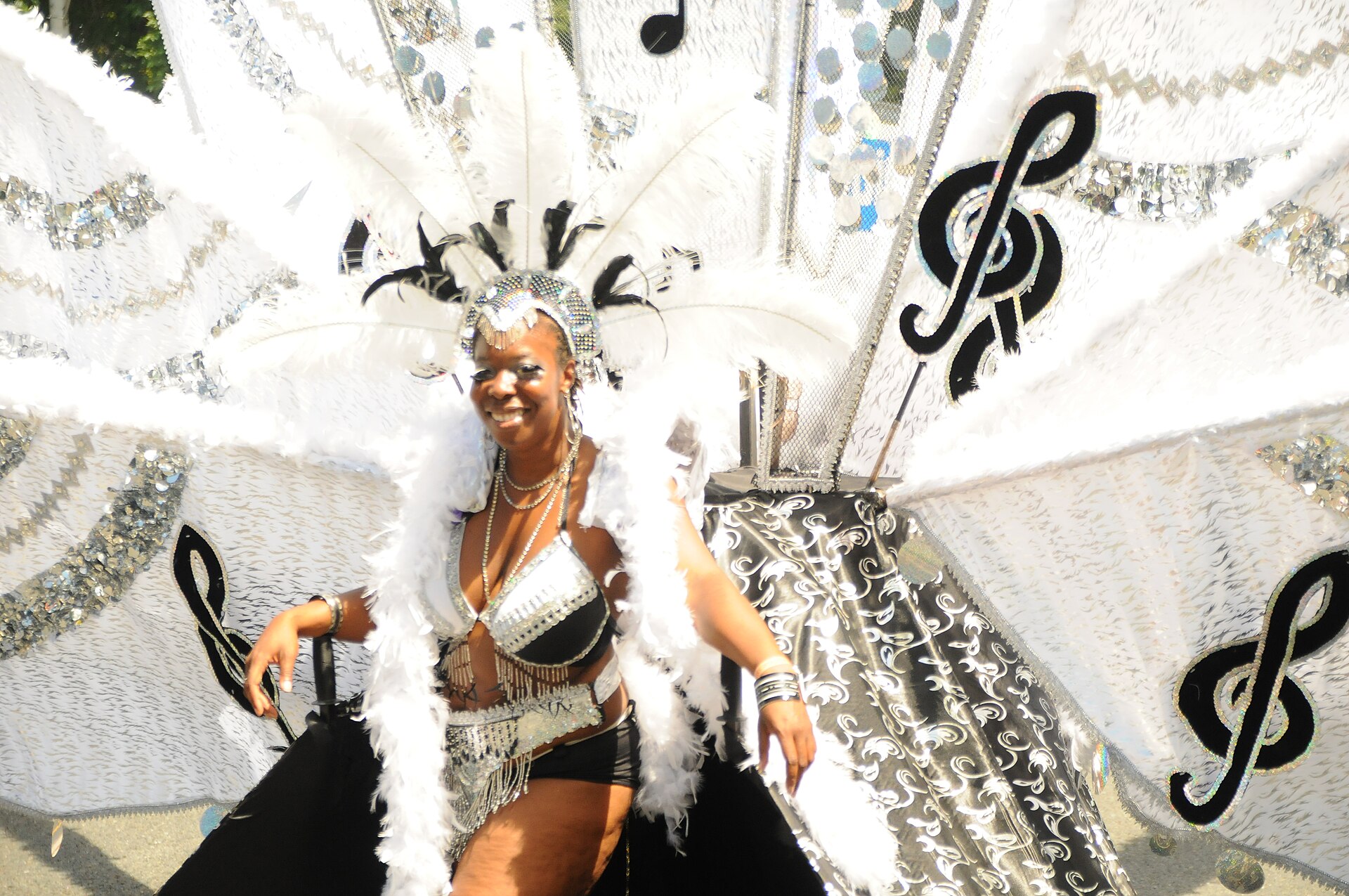 A Toronto Caribana masquerader wears a white feathered costume with silver decorations and large black treble clefs.