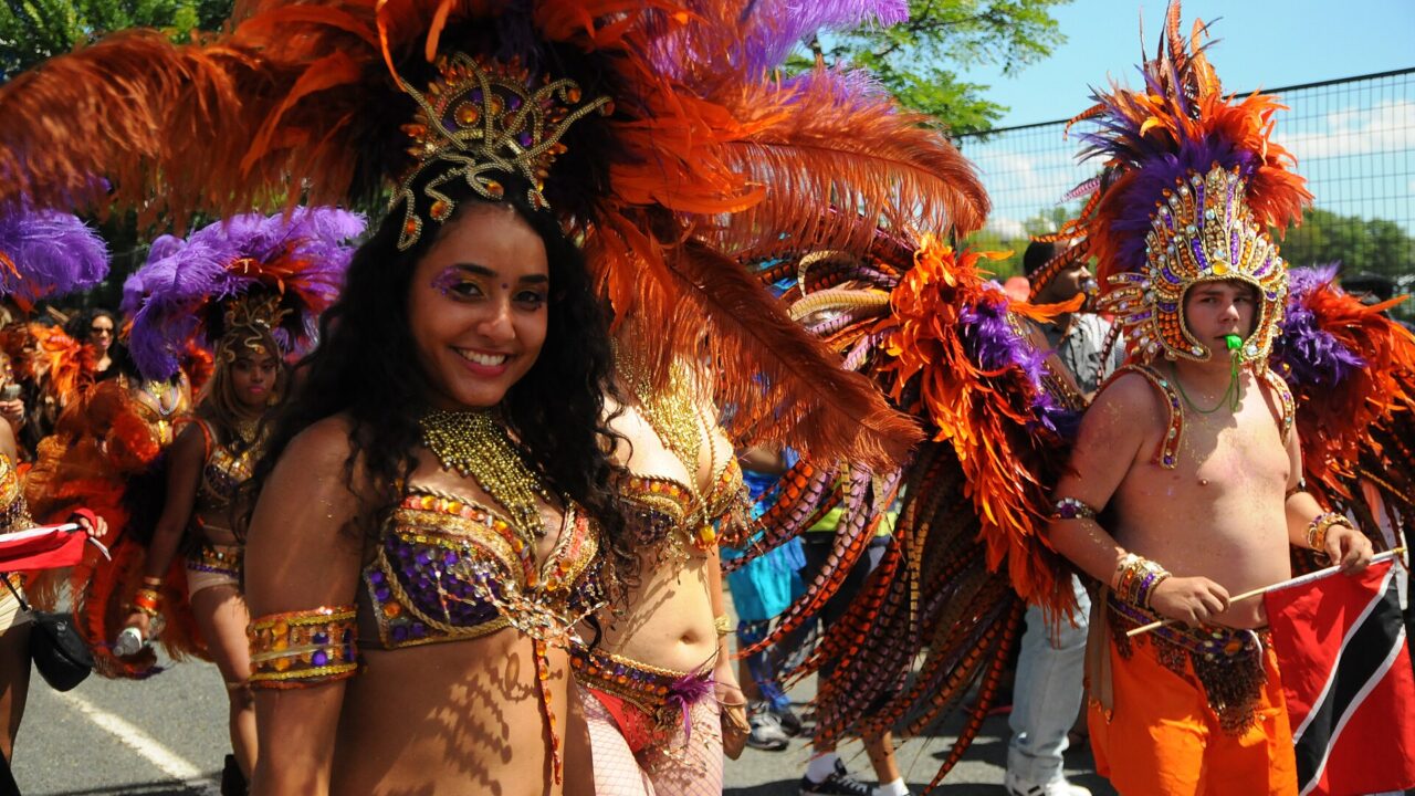Toronto Caribana masqueraders wear orange and purple feathered headdresses and beaded costumes in the sunshine.